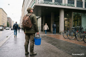 Marjanpoimija seisoo Suomen verotoimiston edessä sininen ämpäri kädessään
